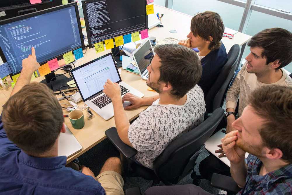 Photograph of a group of developers mob-programming by working together around the one computer