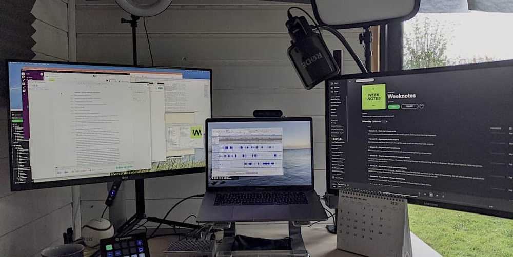 My setup, laptop and two screens at a desk in a shed with a USB Microphone